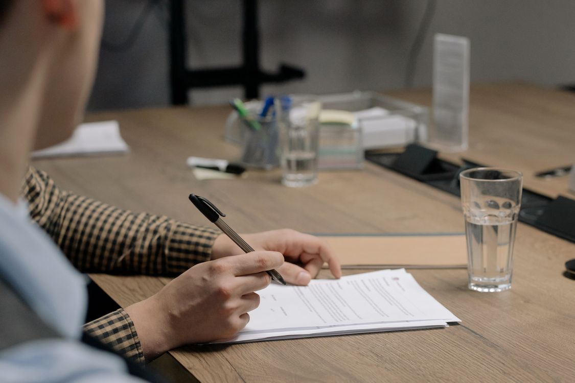 Person in Business-Kleidung unterschreibt ein Dokument an einem Holztisch im Büro